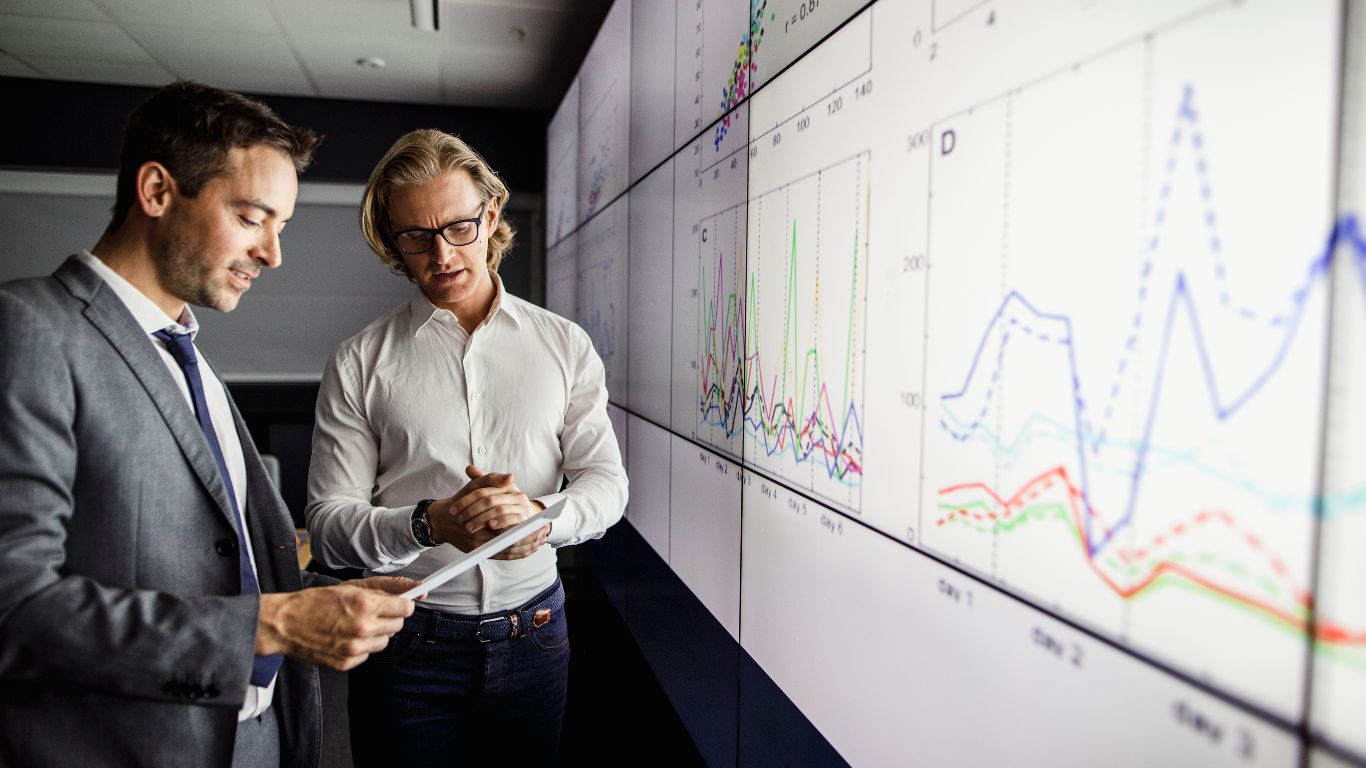 Zwei Experten analysieren Monitoring-Daten und Traffic-Spitzen auf großen Displays – Symbolbild für Performance-Optimierung, skalierbares Web-Hosting mit TYPO3, Shopware 6 Redis und Solr for TYPO3 Websites.