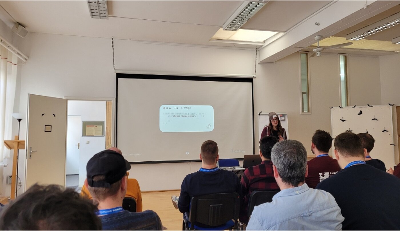 Ein Vortrag vor einer Gruppe Menschen. Auf der Leinwand ist eine mathematische Aufgabe.