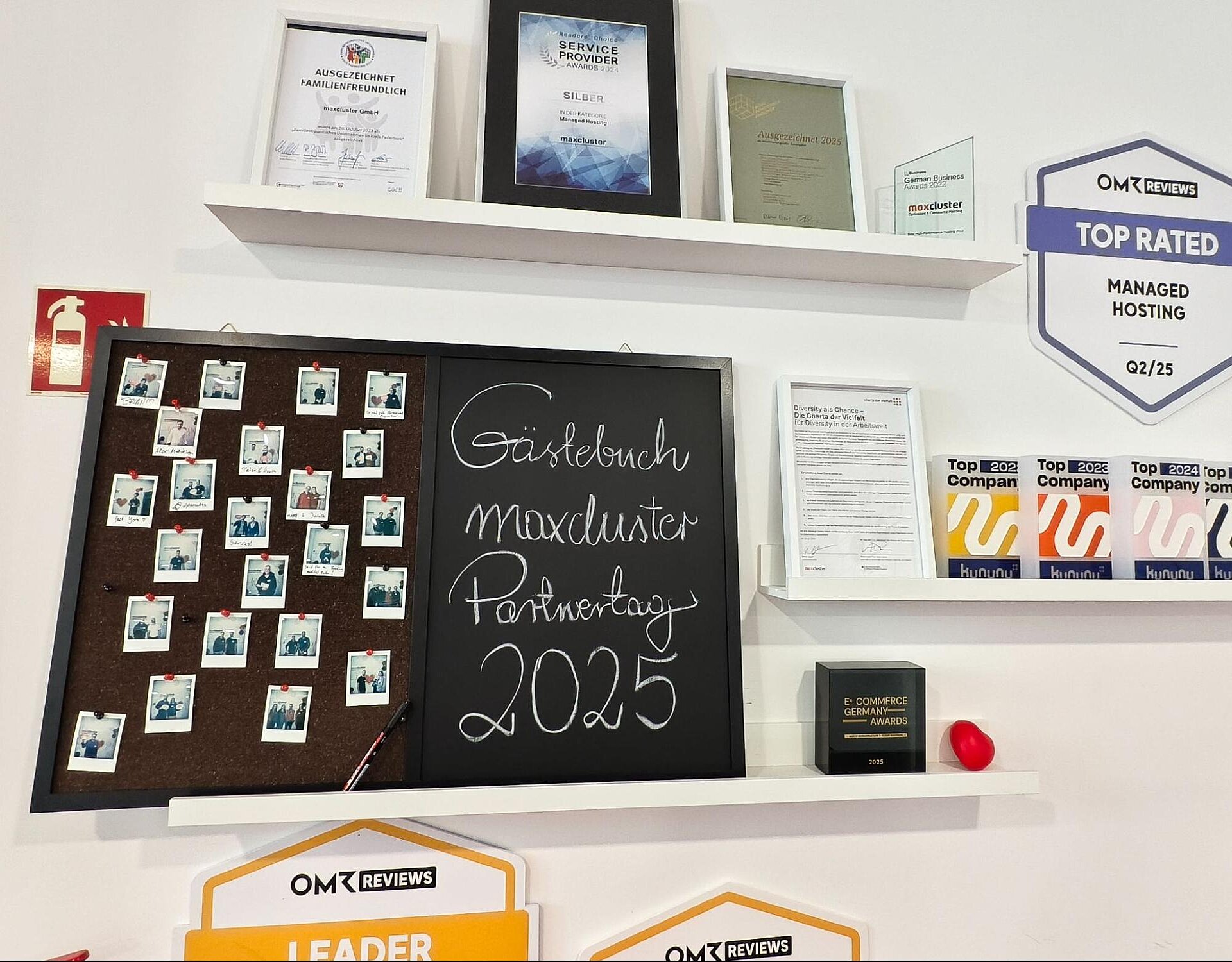 Das Gästebuch des maxcluster-Partnertags 2025 mit Polaroid-Fotos der Teilnehmenden, eingerahmt von Auszeichnungen und Zertifikaten an der Wand.