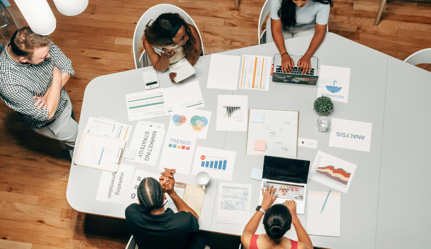 Gruppe von Menschen bei einer Marketingbesprechung mit Laptops, Charts und Dokumenten rund um Analyse, SEO und Automatisierung – aufgenommen von oben an einem Konferenztisch