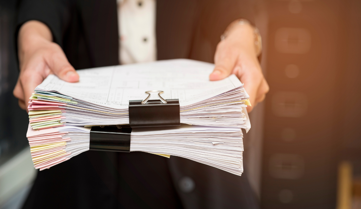 Person hält einen großen Stapel Papierdokumente mit Büroklammern – Symbolbild für Datenschutzdokumentation, Verfahrensverzeichnisse oder DSGVO-Nachweispflichten.